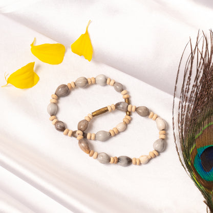 Mala with gray and beige beads on a white surface with yellow leaves and a peacock feather.